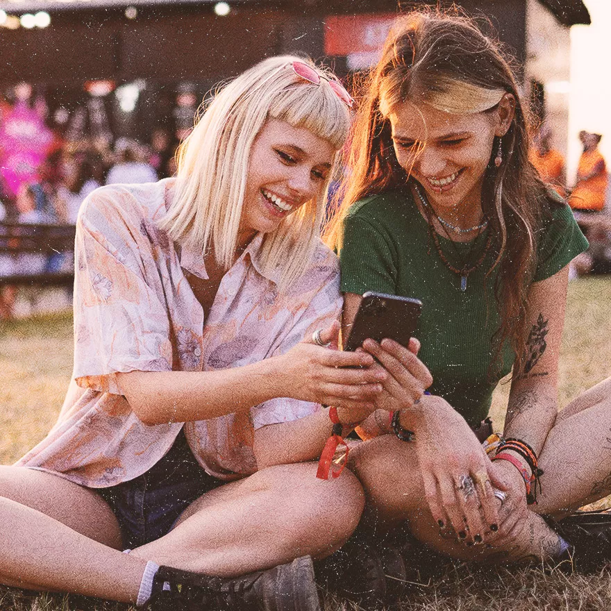Two young women sitting together on the grass at a festival