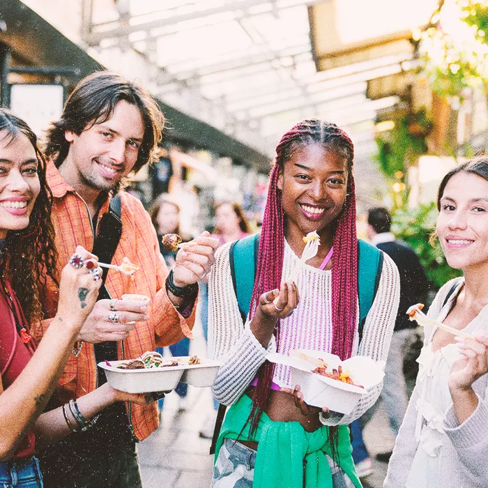 Four people smiling towards the camera while having takeout