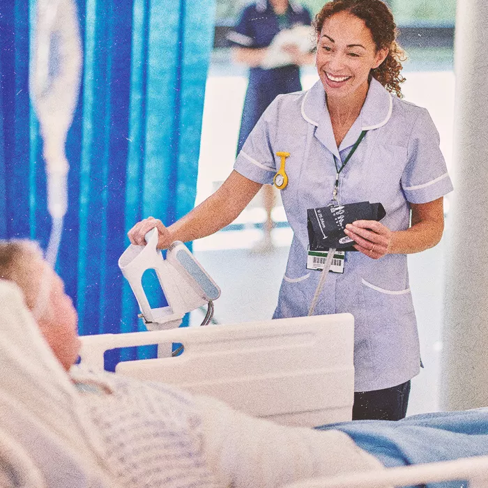 Nurse standing by hospital bed smiling at a patient