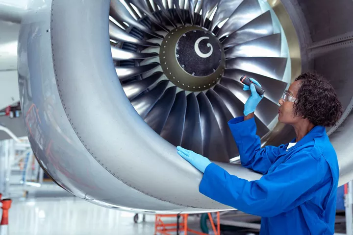 Technician in blue coveralls inspects a jet engine fan with a flashlight.