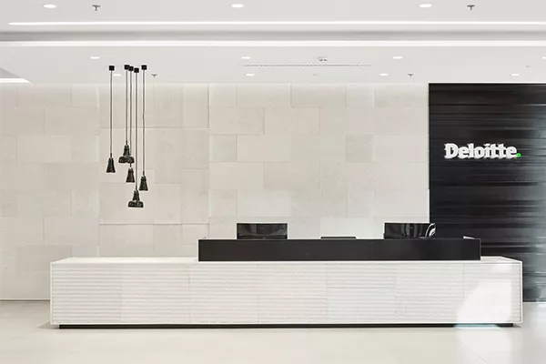 Moderní recepce společnosti Deloitte s bílým pultem a černým logem na stěně