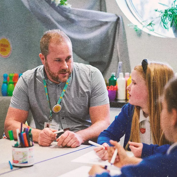 Teacher talking to two students sitting in a classroom