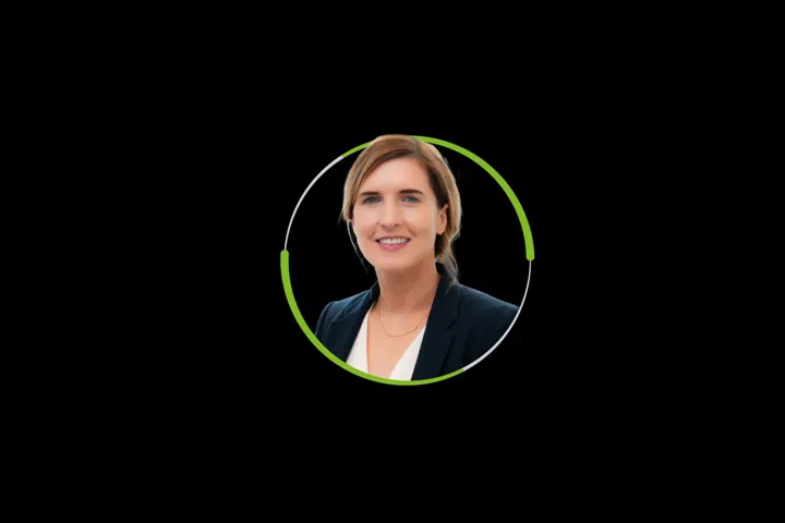 Woman in navy blazer smiling in green-and-white circular frame on black.