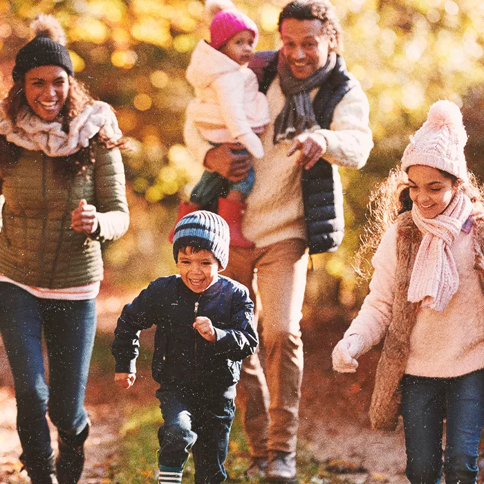 Two smiling adults with three kids running towards the camera outside