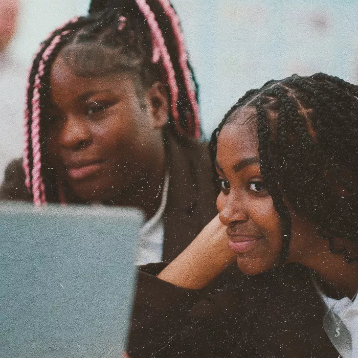 Two smiling students are looking at a laptop