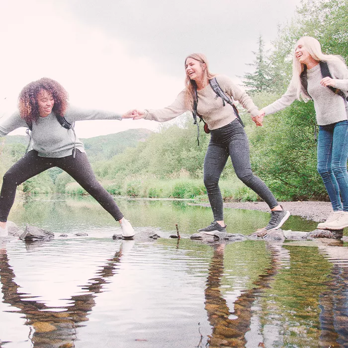 Three young people holding hands while walking on stones across water
