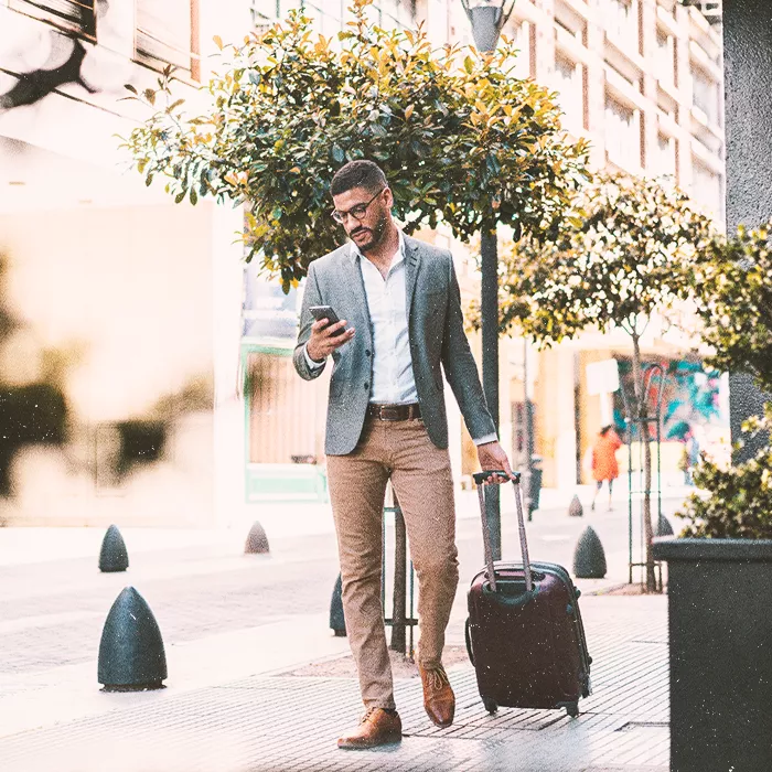 Man walking in the city with a suitcase looking at his phone