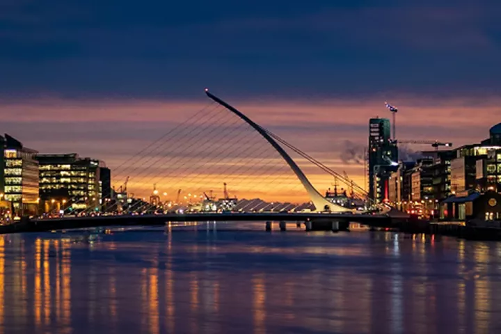Samuel Beckett Bridge at dusk over the River Liffey, Dublin skyline lit up.